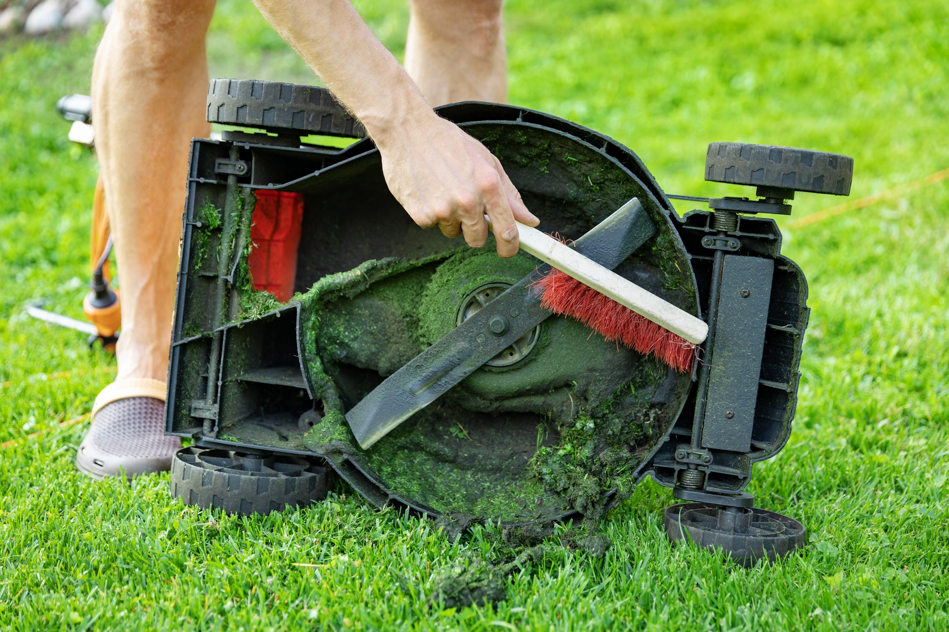 man with brush cleaning lawnmower from old grass